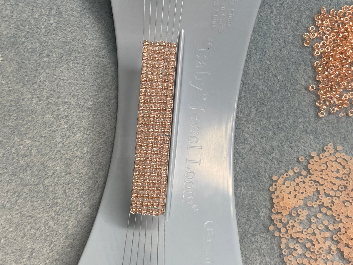 Baby Jewel Loom with Siz 8/0 TOHO Seed Beads warped onto warps. Beads are Rosalina in color.