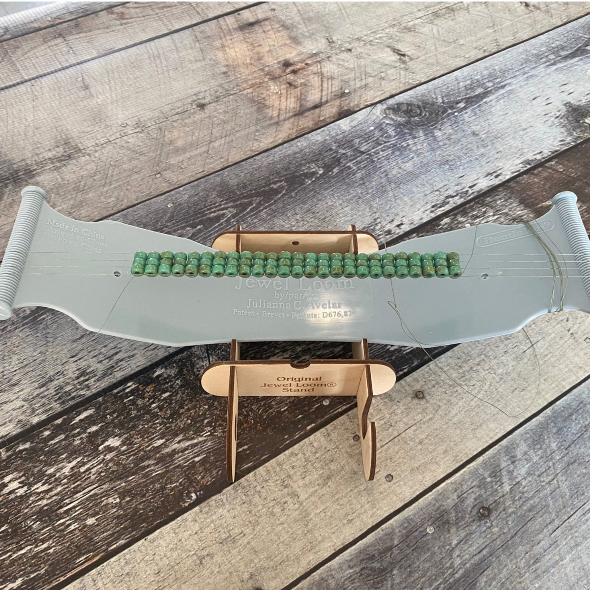 Jewel Loom Stand with Jewel Loom bead Loom laying flat on stand. Photographed on faux wood background in tones of blue grey.