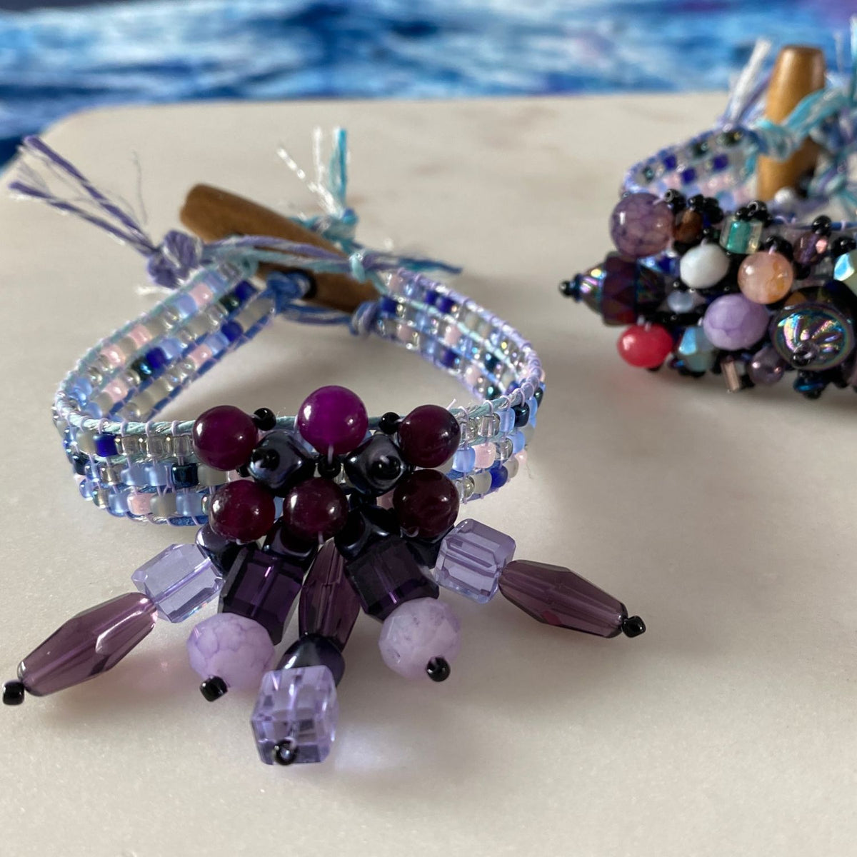 Jewel Loom Jewel Box August 2026 Finished bracelets in shades of purple with varigated hemp cord by Hemptique on a white surface
