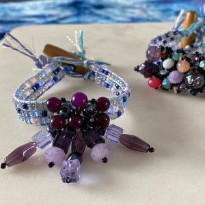 Jewel Loom Jewel Box August 2026 Finished bracelets in shades of purple with varigated hemp cord by Hemptique on a white surface