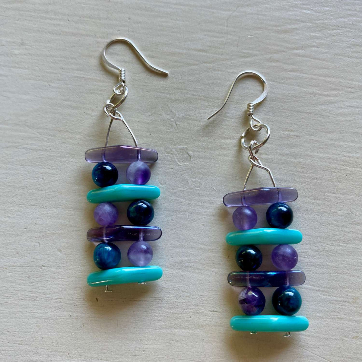 Pair of beaded earrings with blue and purple beads on a light wooden surface