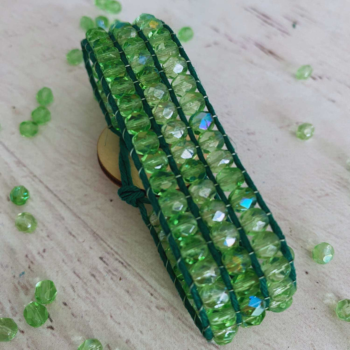 Ultimate Jewel Loom Starter Kit Bracelet finished. Green beads from kit along with green hempcord positioned on a light wooden surface with scattered beads.