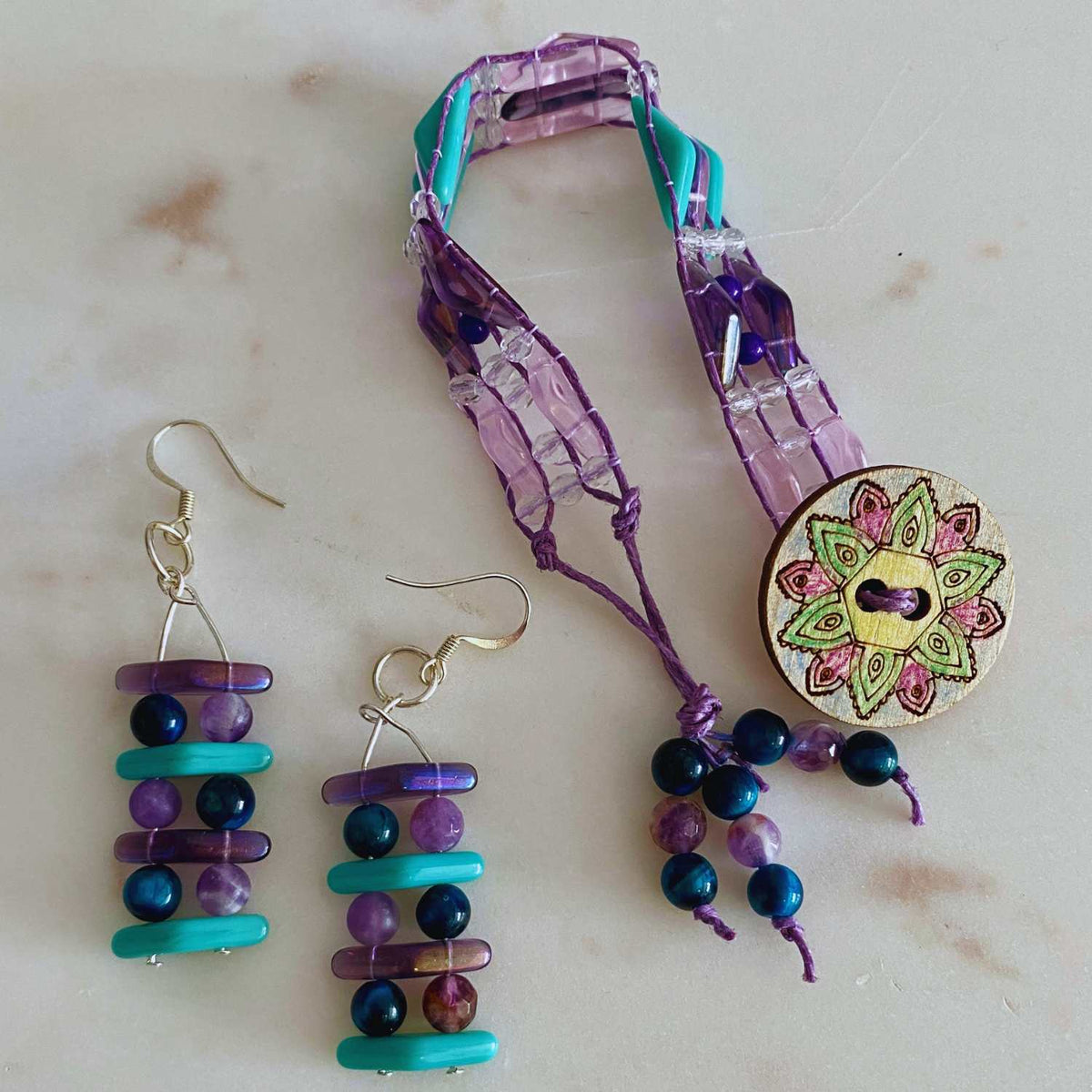 Colorful beaded earrings and a decorative beaded bracelet made with the Amethyst Ocean Bead Kit on a light background