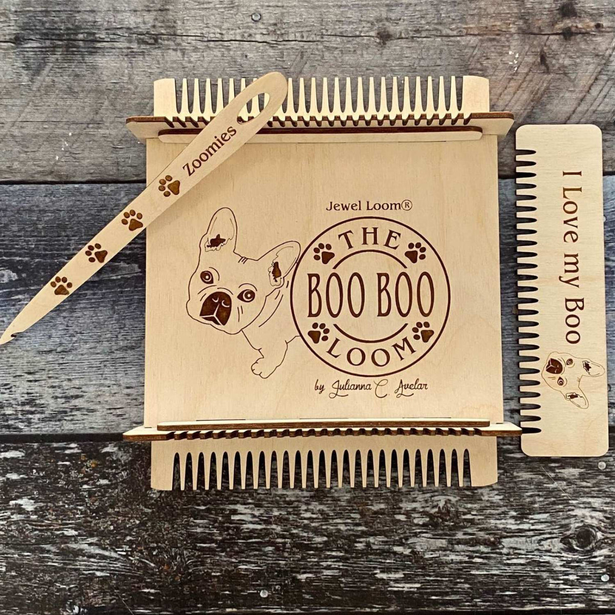 The Boo Boo Loom perfect making coasters laser design with a french bulldog face and the words The Boo Boo Loom with paw prints laser engraving on top of the loo. Wood Needle with the word Zoomies and laser paw prints and a weaving comb with the words, &quot; I love my Boo&quot; and the face of a French Bulldog laser engraved. Photographed on a fauz wood background in hue of blue grey.