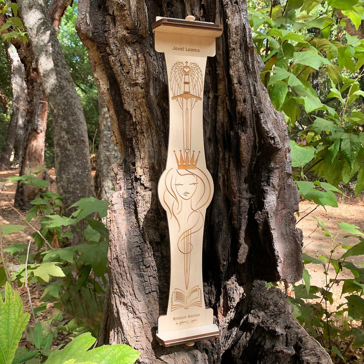 The Large Wisdom Warrior Loom Upright wooden bead loom with intricate laser carvings, placed against a natural background with trees and foliage.