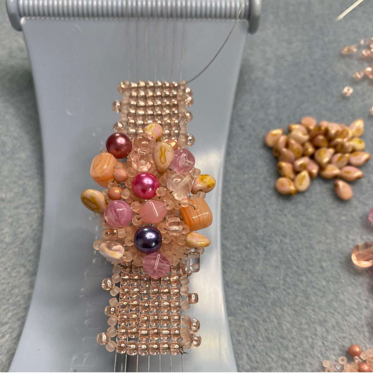 Beaded ring in progress with multicolored beads on a Baby Jewel Loom with grey background