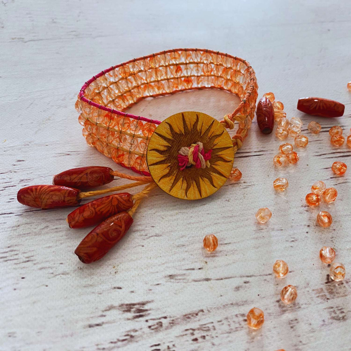 Decorative bracelet with orange beads and a yellow center on a light wooden surface.